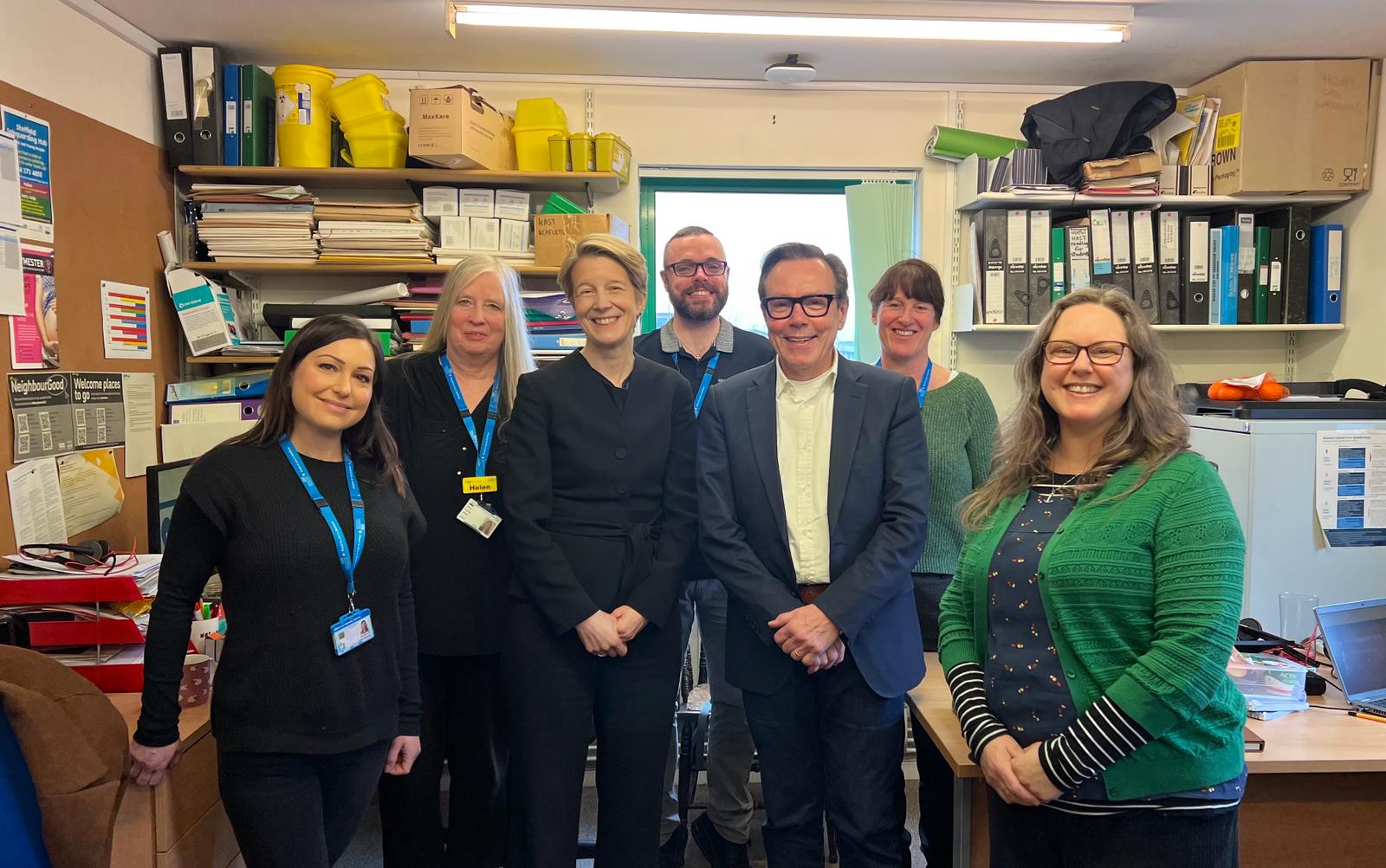 Amanda Pritchard and Tim Kendall stand with NHS workers in a busy office space, with files on shelves and desks in the background