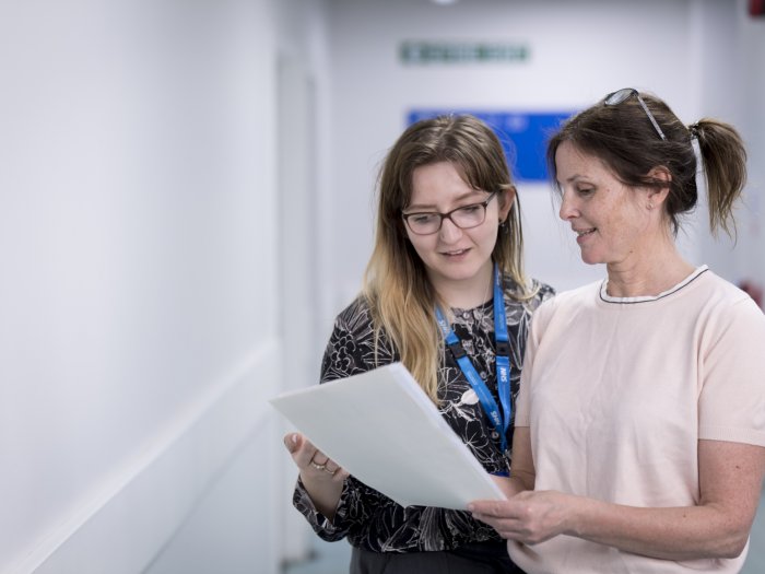 Woman standing with a woman, looking at papers, in a hospital, ward