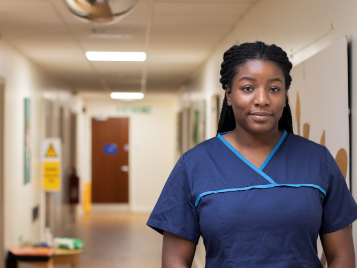 Woman on ward corridor in scrubs looking at camera