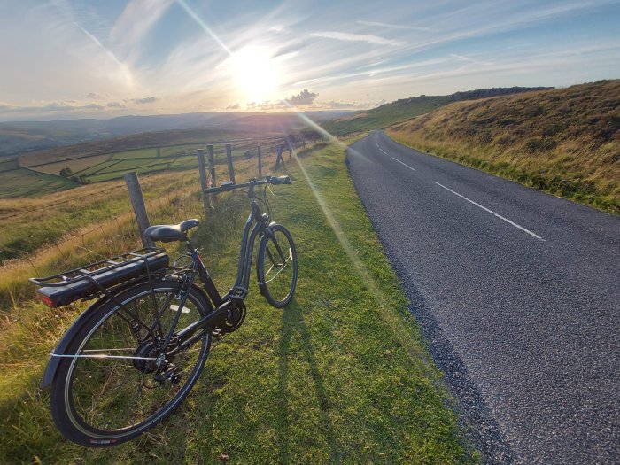 Electric bike on the side of a road in front of rolling green hills and a sunset