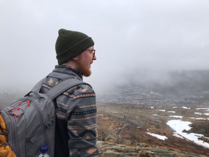 A person wearing a hat and a rucksack looking out at a misty hilly landscape