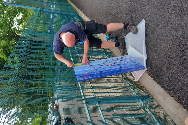 Man measuring a piece of artwork to put on fence