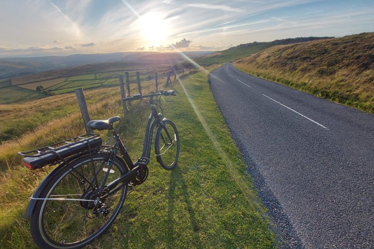 Electric bike on the side of a road in front of rolling green hills and a sunset