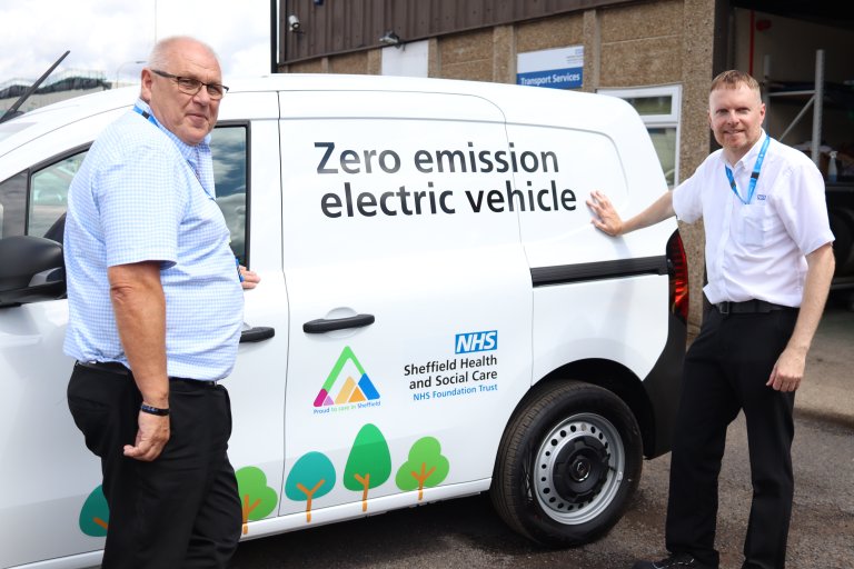 Two people stood in front of white van with livery showing it is an electric vehicle