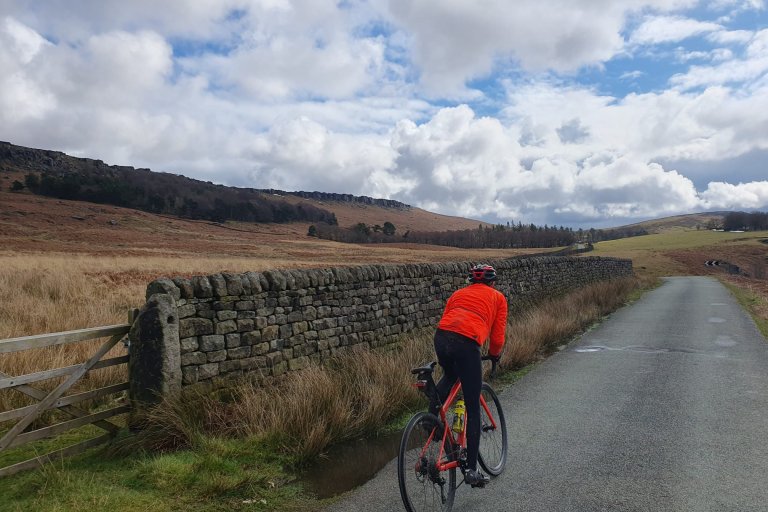 Person in motion cycling along a road below a Peak District edge
