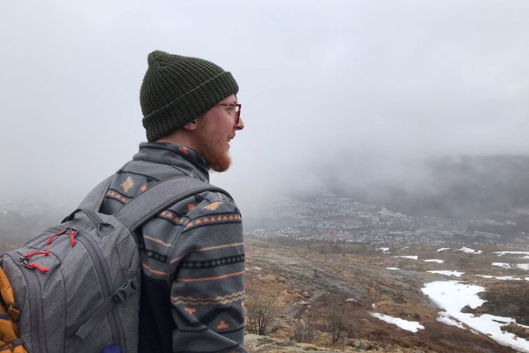 A person wearing a hat and a rucksack looking out at a misty hilly landscape