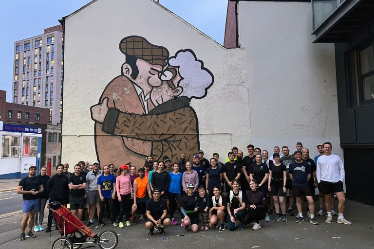 Group of runners in front of a building with a mural on which shows two people kissing