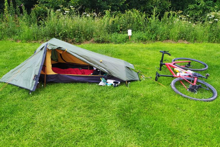 A bike lies next to a small pitched tent on a campsite