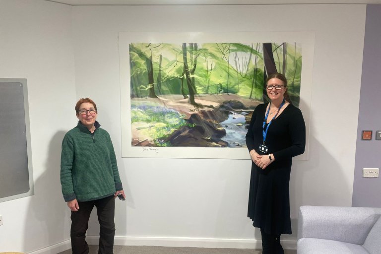 Artist, Jill Ray, and Sharon Mays, chair, stand in front of a work of art on a wall