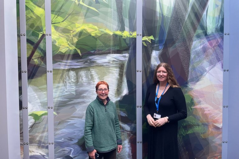 Jill Ray, artist, and Sharon Mays, chair, stand with artwork in the courtyard