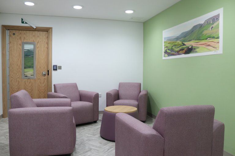 Four chairs sit in a circle around a table, with artwork on the wall above them