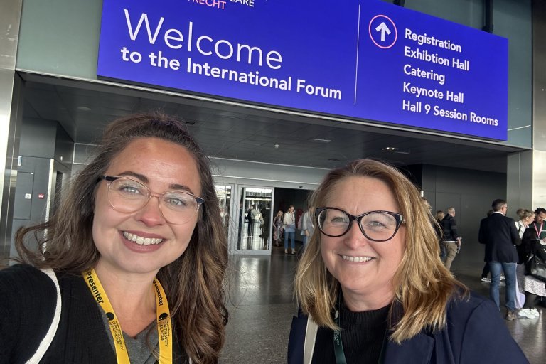 People smiling in front of a welcome sign at a conference