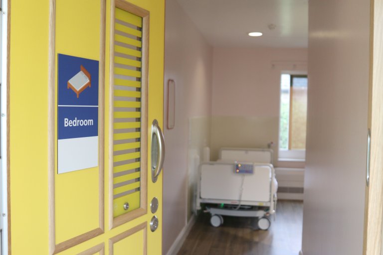 Bright yellow bedroom door open onto a medical but homely bedroom
